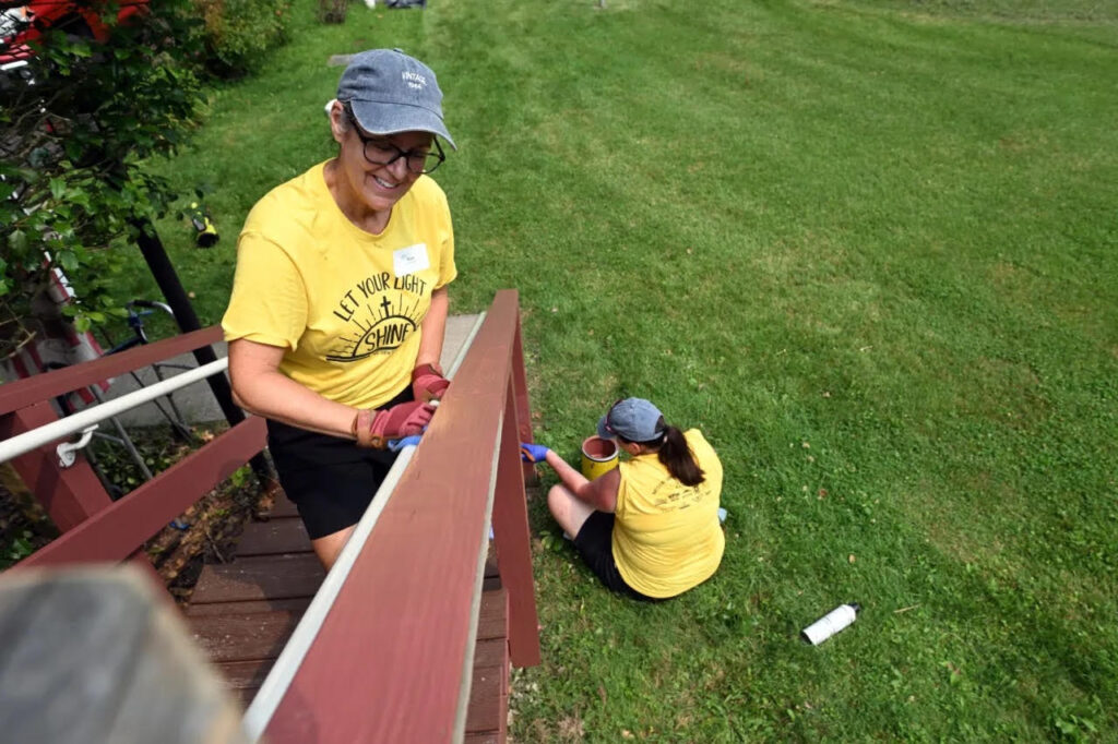 Susie Kersge of Douglassville cleans prepares a railing for painting as Dawn Fear of Stowe paints at a home in Amity Township during the Mission Trip Birdsboro on Thursday, July 16, 2026. (BILL UHRICH/READING EAGLE)